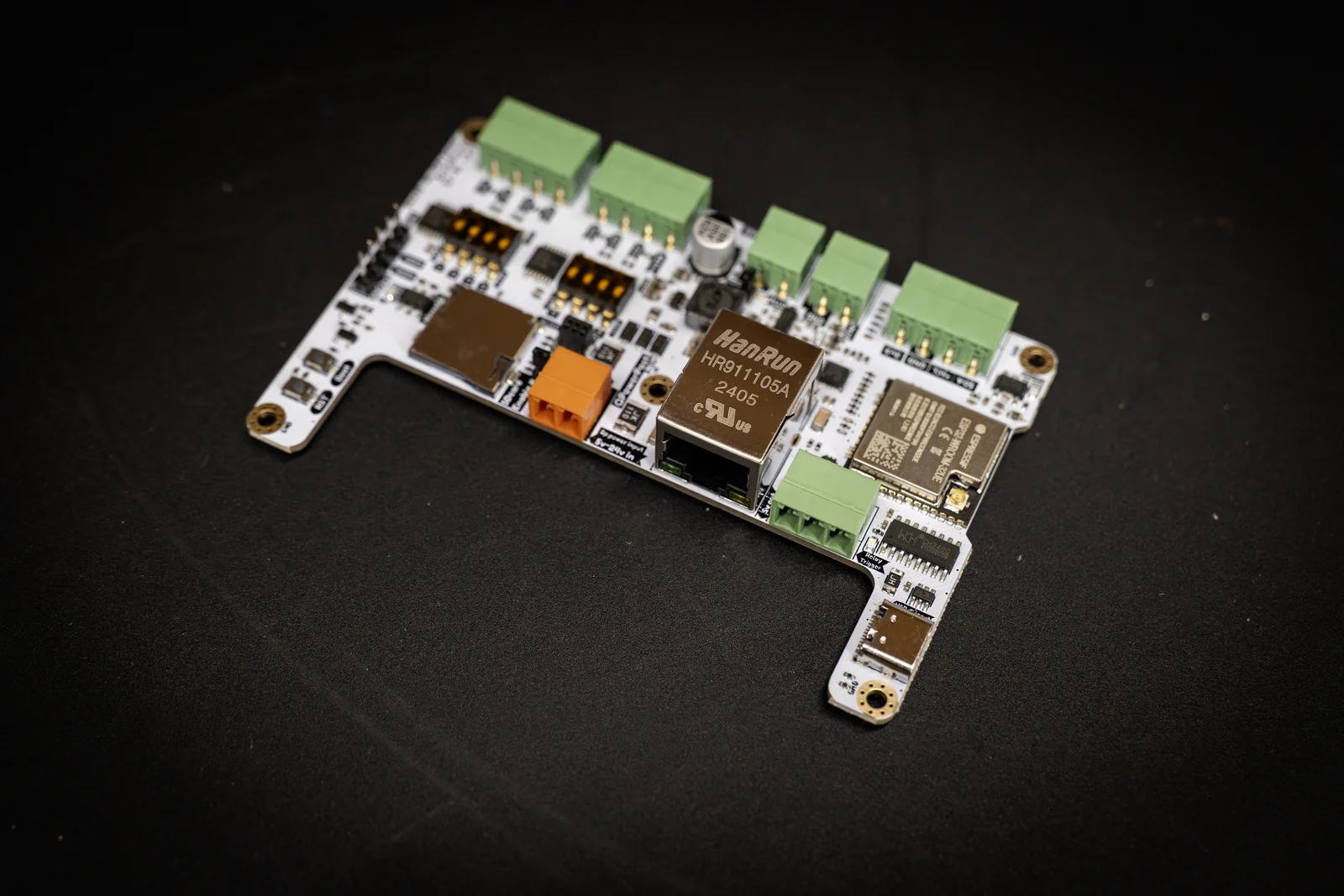 Brainboard-32-8L v2 at an angle on a dark surface, ESP32 module and green terminals in focus