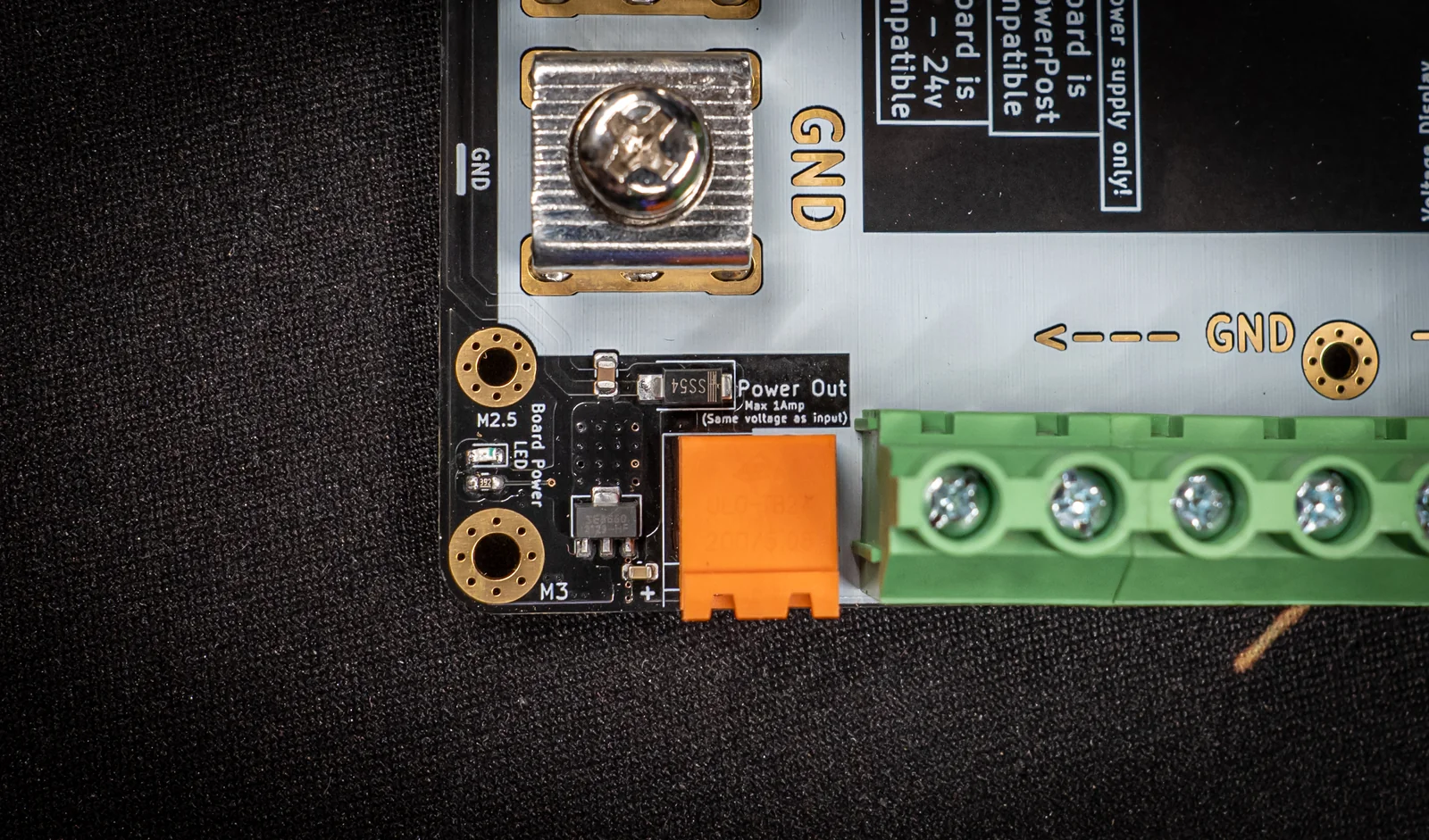 Macro of the Power-5 brainboard-feed area: orange Power Out terminal beside an M5 ground stud and green output terminals