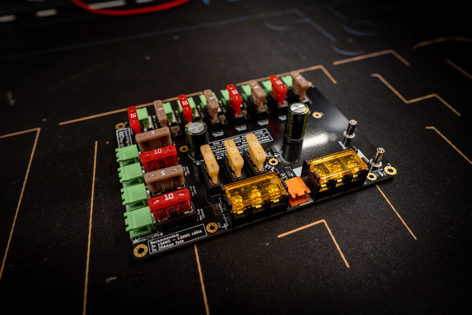 Dig-Octa powerboard at an angle: rows of red and tan blade fuses, green pluggable outputs and amber-covered busbar input terminals on black PCB