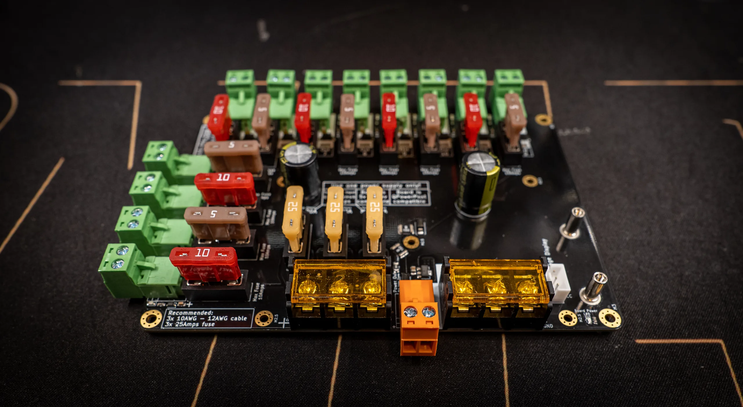 QuinLED Dig-Octa Power-5 powerboard on a dark workbench: 12 green pluggable fused outputs, rows of blade fuses, amber-covered busbar input terminals and orange brainboard feed